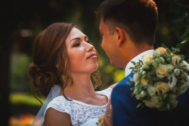 Gelin ve damat, doğa parkında sarılıp öpüşüyor.