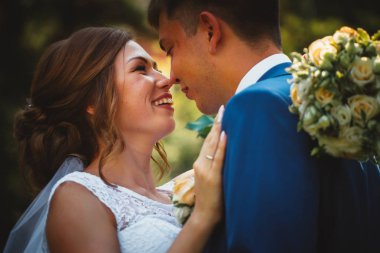 Gelin ve damat, doğa parkında sarılıp öpüşüyor.