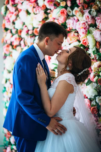 Όμορφη νύφη και γαμπρός στο φόντο ενός τοίχου με λουλούδια — Φωτογραφία Αρχείου
