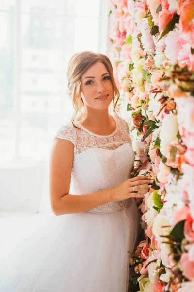 Schöne Braut auf dem Hintergrund einer Wand aus Blumen — Stockfoto