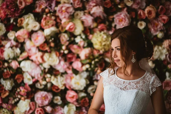 Schöne Braut auf dem Hintergrund einer Wand aus Blumen — Stockfoto