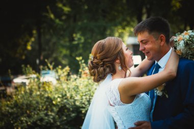 Gelin ve damat, doğa parkında sarılıp öpüşüyor.