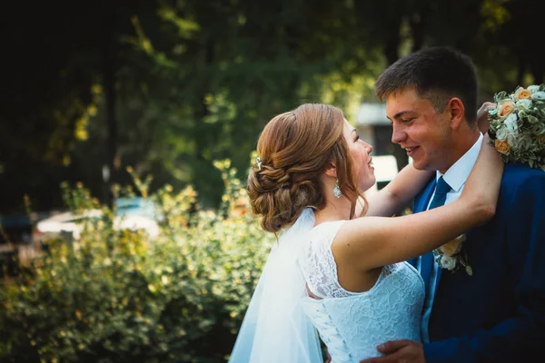 Gelin ve damat, doğa parkında sarılıp öpüşüyor.