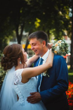 Gelin ve damat, doğa parkında sarılıp öpüşüyor.