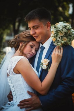 Gelin ve damat, doğa parkında sarılıp öpüşüyor.