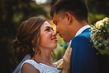 Gelin ve damat, doğa parkında sarılıp öpüşüyor.