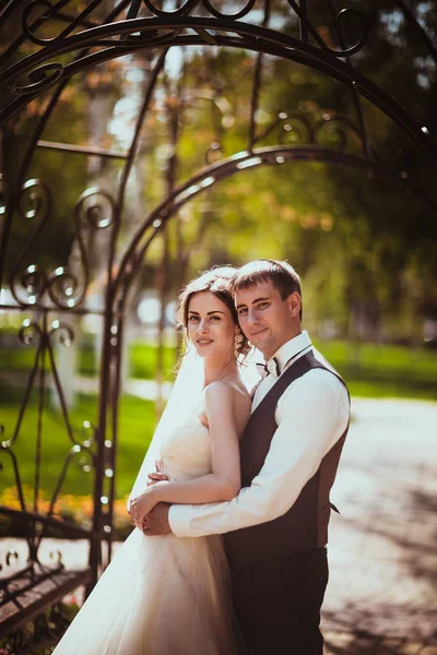 The bride and groom in the park arch — Stock Photo, Image