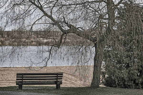 Spätherbst am Fluss: ein leerer Strand und eine Bank. — Stockfoto