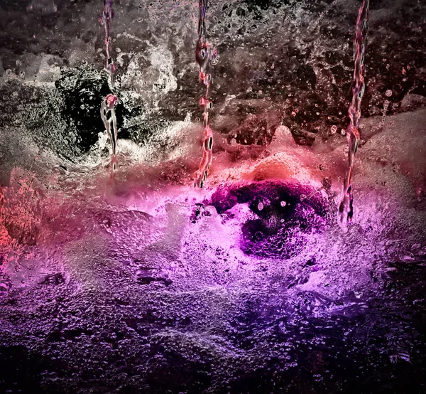 Güzel kırmızı ışık ile aydınlatılmış, düşen ve köpüren su jetleri. Yakın çekim sunar.