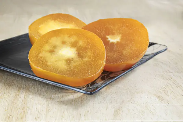 The slices of persimmon on the table on a glass dish. — Stock Photo, Image