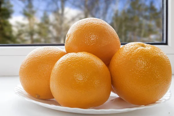 Oranges on a plate on the sill of the window. — Stock Photo, Image