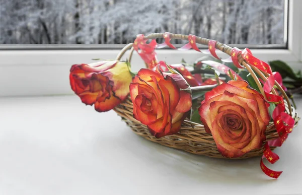 Beautiful large roses with leaves in a wicker basket on the windowsill. — Stock Photo, Image