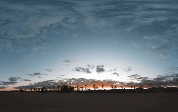 夕阳西下的天空被夕阳西下的太阳照亮了 地平线上有绿洲的沙漠景观 — 图库照片