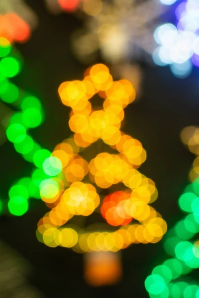 The soft focus of the background - bokeh of bright yellow and green contours of the lights of a Christmas tree shape of sparkling decorations and stars at the top. — Stock Photo, Image