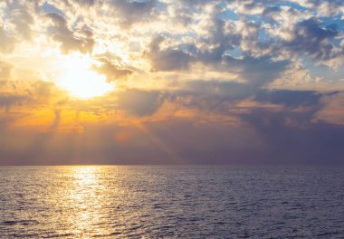 Denizde dramatik bulutlarla birlikte doğal tropik gün batımı. Günbatımı gökyüzü, okyanusun üzerinde güneş tarafından aydınlatıldı. Suya renkli ışınlar yansıdı. Seyahat arkaplanı.
