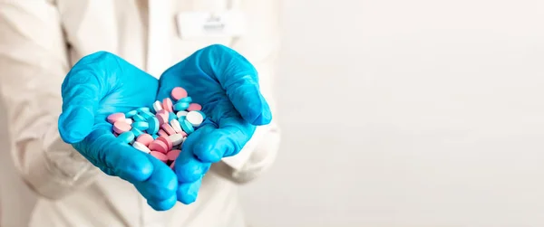 Närbild läkarna händerna i blå medicinska handskar sträcks fram och hålla piller, medicin, vitaminer och antibiotika för behandling av hälsa på ljus bakgrund, kopiera utrymme. — Stockfoto