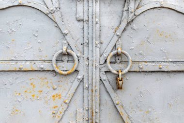 Kapalı eski bir metal kapı ya da kapı parçası. Yuvarlak memeleri ve paslı asma kilidi var. Yakından eski püskü, pörsümüş demir desenli, üzerinde kırmızı pas lekeleri olan bir boya tabakası. Arkaplan.