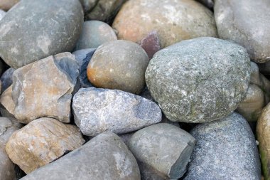 Okyanus üzerindeki plajın yüzeyi farklı boyutlarda gri ve kahverengi renkli büyük parlak yuvarlak taşlarla kaplıdır. Deniz kıyısındaki büyük kaya veya çakıl taşlarının doğal arkaplanı..