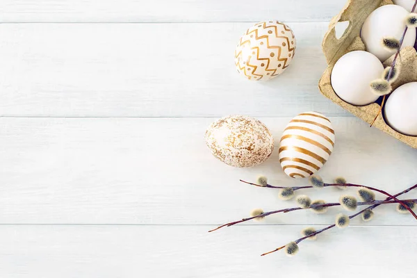 Easter morning. Unpainted and painted chicken eggs in a cardboard box with a willow branch on a white table close-up, top view. Festive background, top view, copy space.