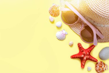 Güneş gözlüğü, hasır şapka, güneş gözlüğü ve deniz taşlı deniz kabukları. Yaz tatili geçmişi. Yaz zamanı, seyahat, plaj, turizm konsepti. Kopyalama alanı olan güneşli sarı arkaplan.