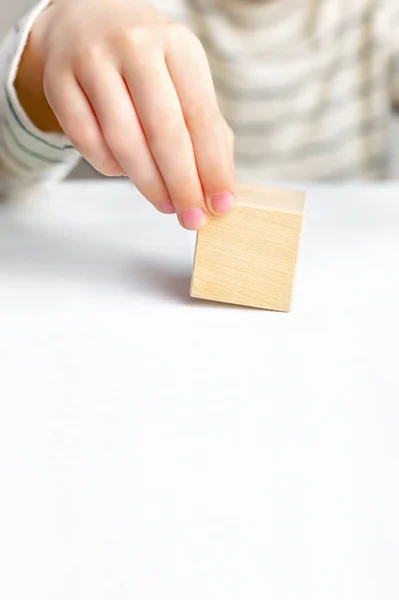 Close-up of a childs hand holds a wooden block empty cube on a white table background, copy space. The concept of choice, dream, decision making, solve a problem, find idea and answer.