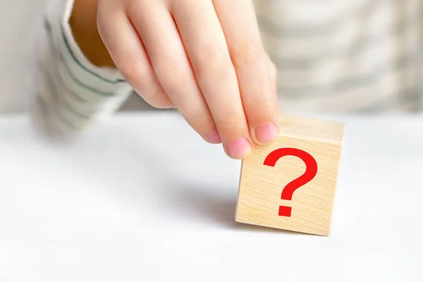 Close-up hand of a child holding the question mark on wooden block cube on light table background, copy space. The concept of choice, decision making, solve a problem, find answer, learn the unknown.