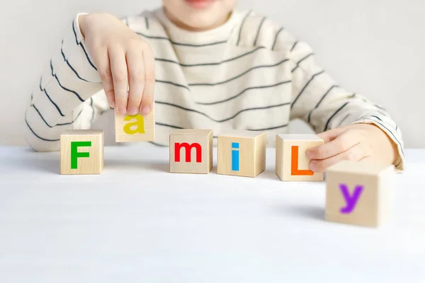 Childs 'ın elleri ahşap küpleri renkli alfabeyle tutarak aile kelimesini beyaz bir masada oluşturdu. İlgi, ebeveynlik, güven ve ebeveynlerin karşılıklı anlayışı. Arkaplan, boşluğu kopyala.