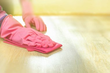 Temizlik kavramı. Pembe eldivenli bir kadın eli yumuşak bir bez tutar, ahşap zemini tozdan ve çamurdan siler. Ev temizliği, hafif kaplamaların yüzey temizliği. Kopyalama alanı olan arkaplan.