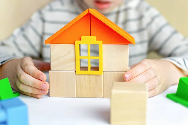 Close up of childs hands build a house of wooden cubes and blocks constructor. Playing toddler, boy or girl at home. Parenting, safety, education, insurance, real estate and mortgage financial concept