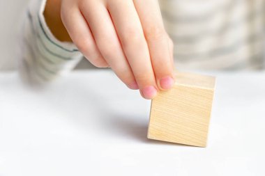 Çocukça bir el, beyaz bir masa zemininde boş bir tahta kübü tutuyor, kopyalama alanı. Seçim, rüya, karar verme, bir sorunu çözme, cevabı bulma kavramı..