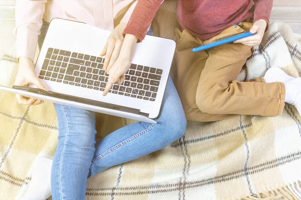 Mom holds a laptop and shows her son the screen. A young woman and boy on the plaid. Home schooling, distance learning, remote work, freelance, work among children, quarantine, balance.