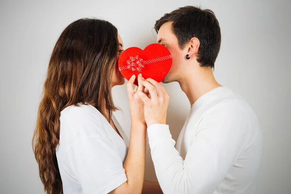 Pareja joven a punto de besarse detrás de una caja de regalo en forma de corazón — Foto de Stock