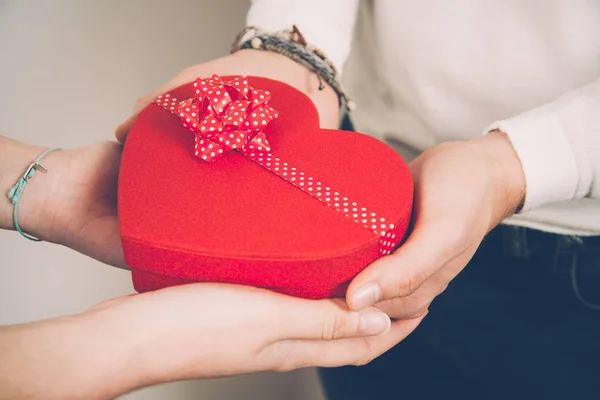 Manos de una pareja sosteniendo una caja de regalo en forma de corazón rojo — Foto de Stock