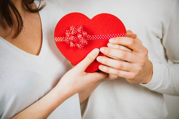 Händerna på ett par holding ett rött hjärta formad presentförpackning — Stockfoto