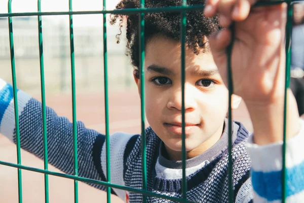 Pequeño niño apoyado en la valla de metal del patio de recreo — Foto de Stock