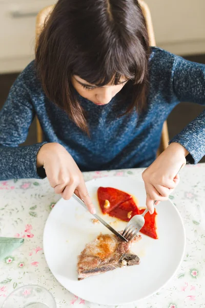 Little girl eating pork chop with peppers — Stock Photo, Image