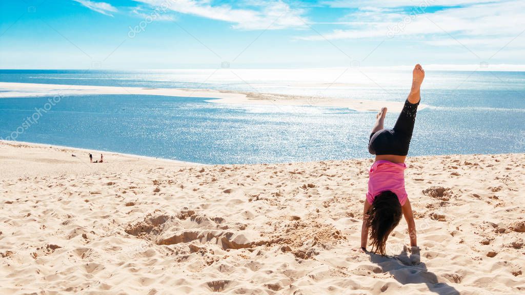 Happy little girl doing a handstand on the beach