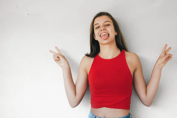 Muchacha adolescente divertida haciendo señal de victoria sobresaliendo de su lengua —  Fotos de Stock