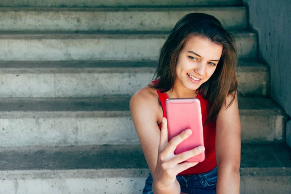 Menina adolescente bonito sorrindo em seu smartphone — Fotografia de Stock