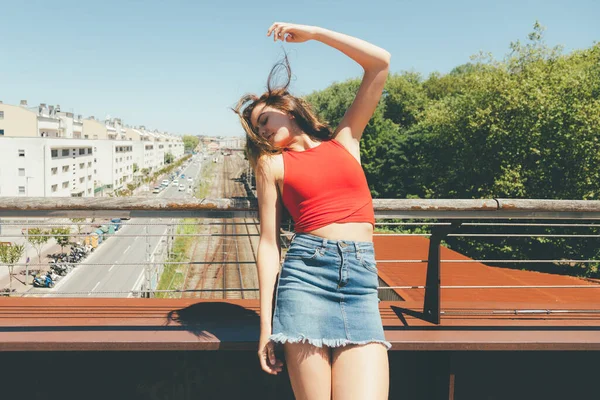 Joven hermosa mujer tomando el sol en un puente sobre la ciudad —  Fotos de Stock