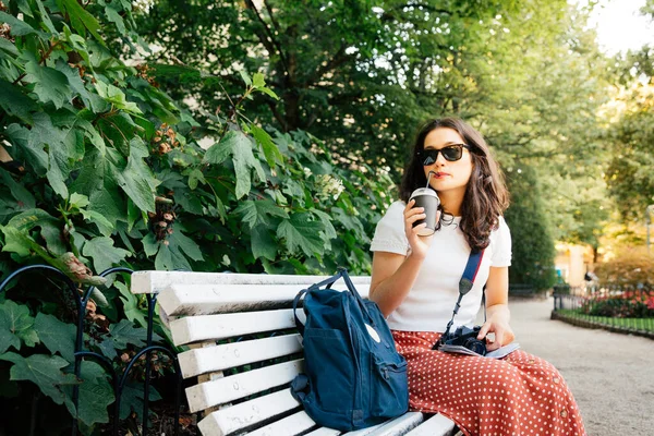 ヨーロッパの街を訪れながら公園でアイスコーヒーを飲んでいる幸せな観光客の女性 — ストック写真