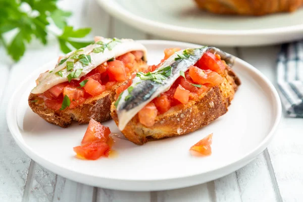 Delicious spanish tapa with marinated anchovies in vinegar, fresh tomato, olive oil and parsley on slices of toasted bread