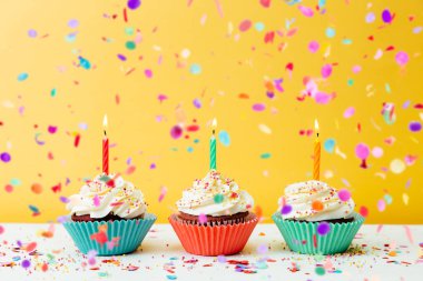 Sarı arka planda mumları ve konfetisi olan üç renkli doğum günü keki.