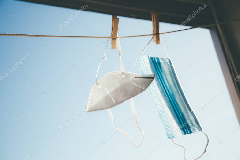 Two facial protective masks of different types hanging in the sun to disinfect