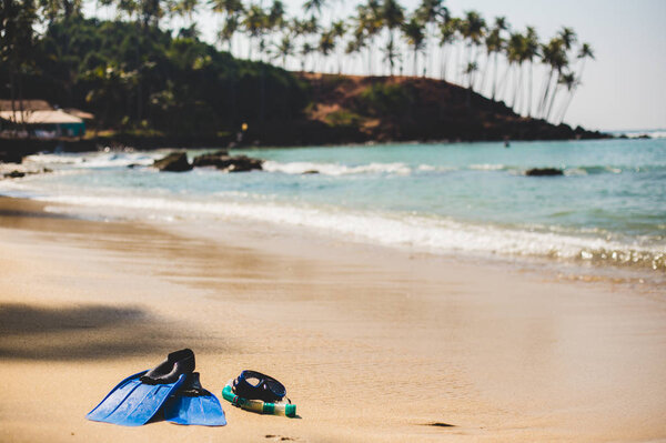 Blue swimming flippers with mask and tube on sand beach on the palm background.