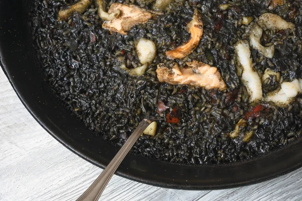 Black paella with cuttlefish ink and seafood in a black pan in a Spanish restaurant. A traditional dish of Spanish cuisine. Delicious family dinner at the restaurant.