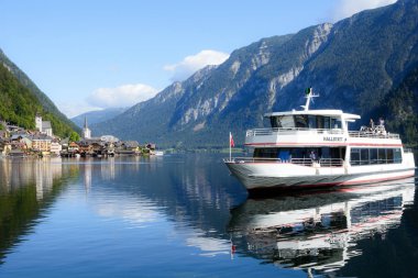 Hallstatt, Avusturya, Eylül 2019. Avusturya Alpleri 'nin ünlü dağ köyü sıcak bir sonbahar gününde. Göldeki eğlence teknesi. Yansıma. Avusturya 'nın pitoresk yerlerine seyahat etmek.