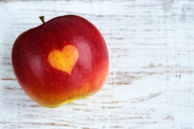 Masada kalp mührü olan kırmızı elmalar. Organik meyvelerin üzerine portakal rengi kalp. Parmak izleriyle meyve yetiştiriyor. Yakın plan.