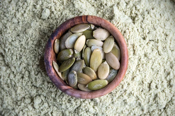 İçinde kabak çekirdeği olan bir kase, kabak unuyla birlikte koyu bir arka plan ve kraft kağıdıdır. Sağlıklı bir yaşam tarzı için ürünler. Buğday ununa bir alternatif..
