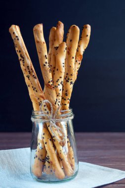 Geleneksel İtalyan ince çıtır Grissini çubukları ve siyah arka planda cam bir kavanozda siyah susam tohumu ve peynir. İtalya 'nın ulusal mutfağı.